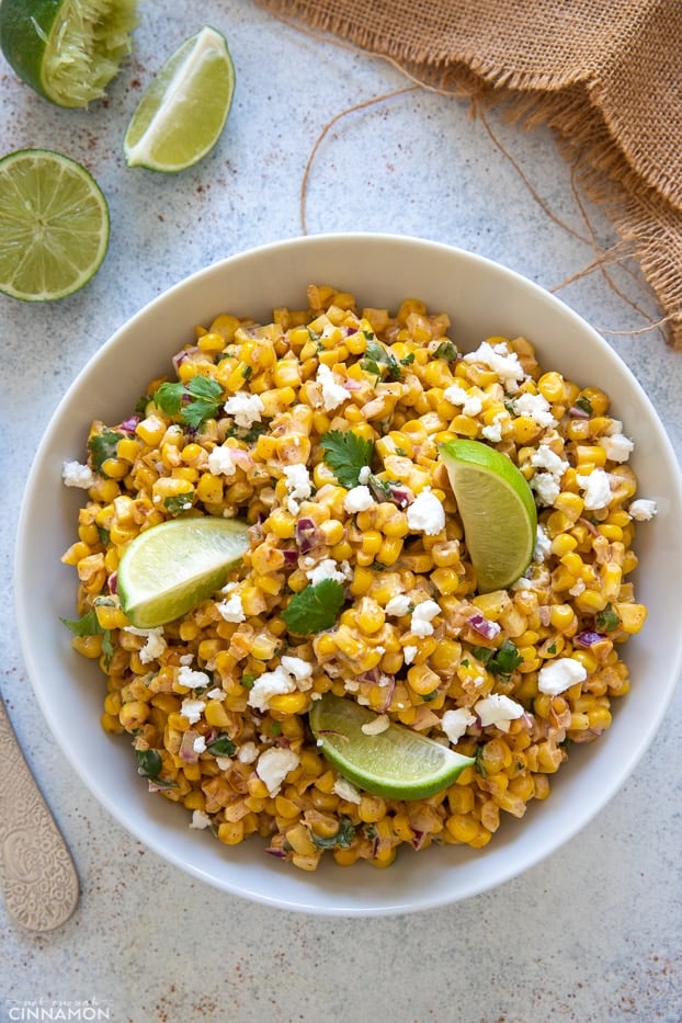 overhead shot of a bowl of Mexican Street Corn Salad with cotija cheese and lime wedges