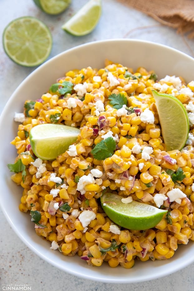side view of a bowl of healthy Mexican Street Corn salad with lime wedges and cotija cheese