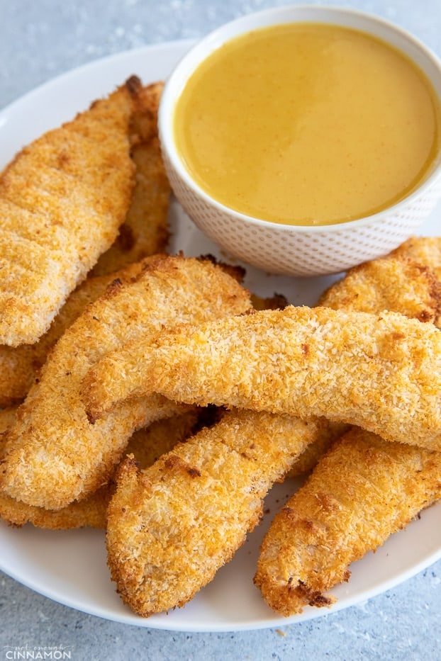 a plate with baked chicken tenders next to a small bowl with honey mustard dipping sauce