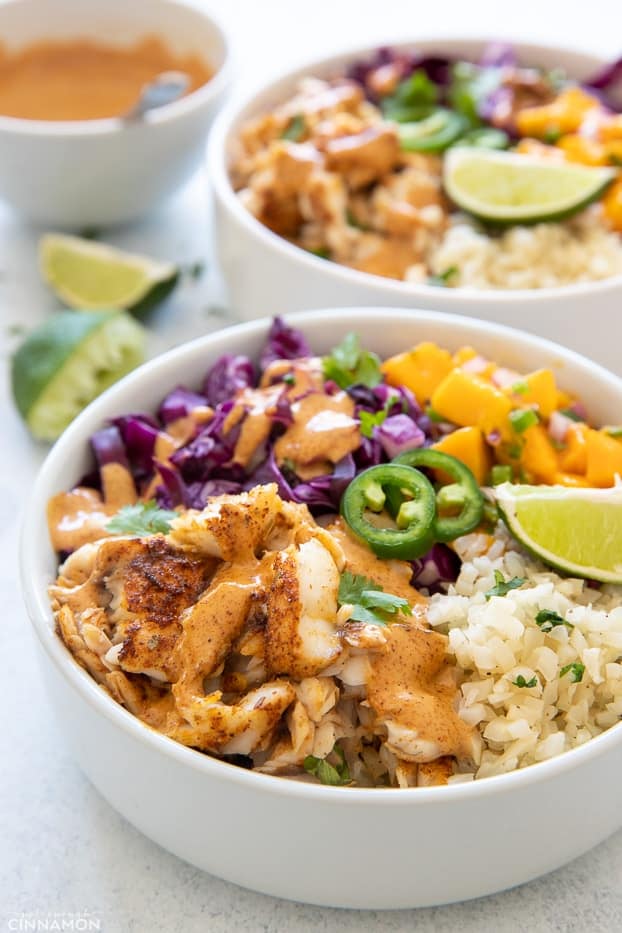 side view of a healthy fish taco bowl with cilantro lime cauliflower rice and baked fish fillet drizzled with chipotle mayo