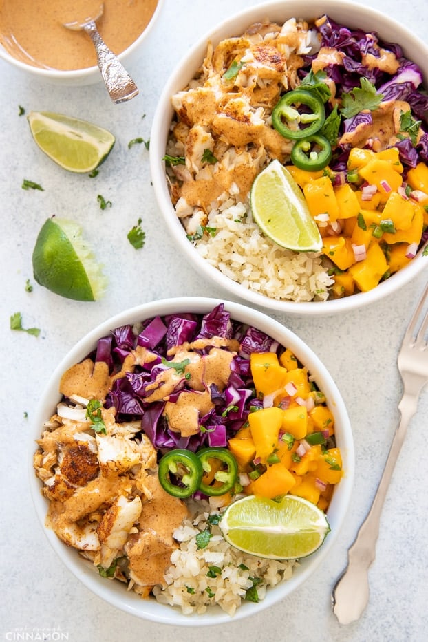 overhead shot of two healthy fish taco bowls with baked white fish, mango salsa, slaw and cauliflower rice