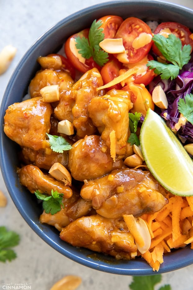 overhead shot of a Thai peanut butter chicken bowl served with chopped peanuts and lime wedges