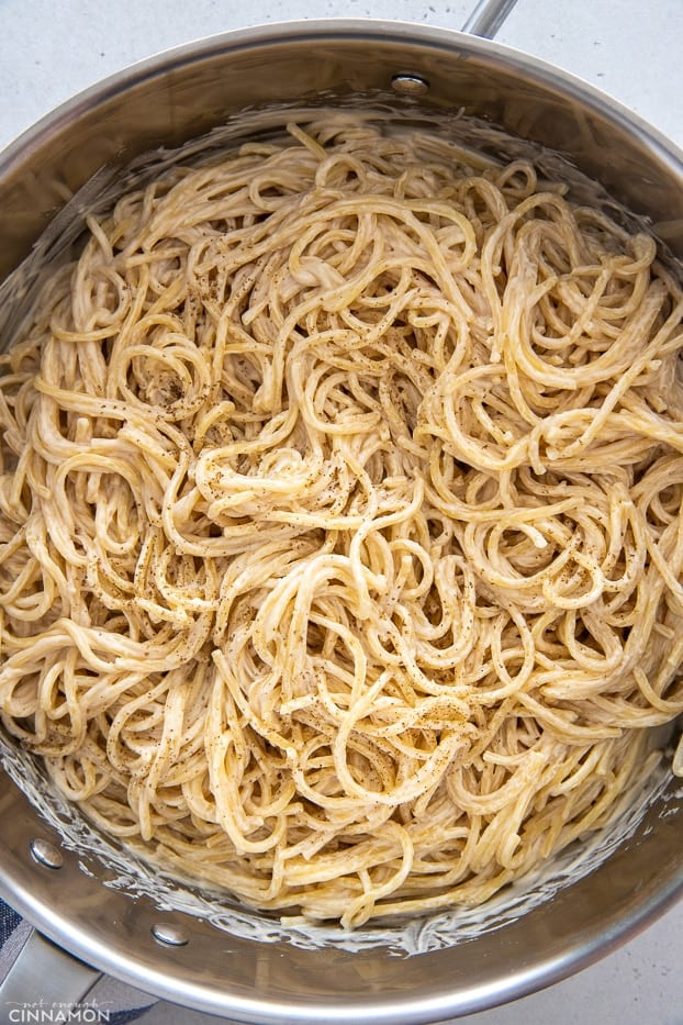 a pot with pasta tossed with creamy lemon tahini sauce and seasoned with pepper