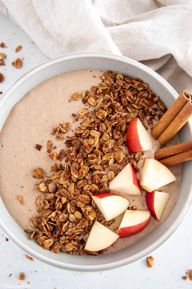 overhead shot of a healthy vegan apple pie smoothie bowl topped with cinnamon sticks granola and apples 