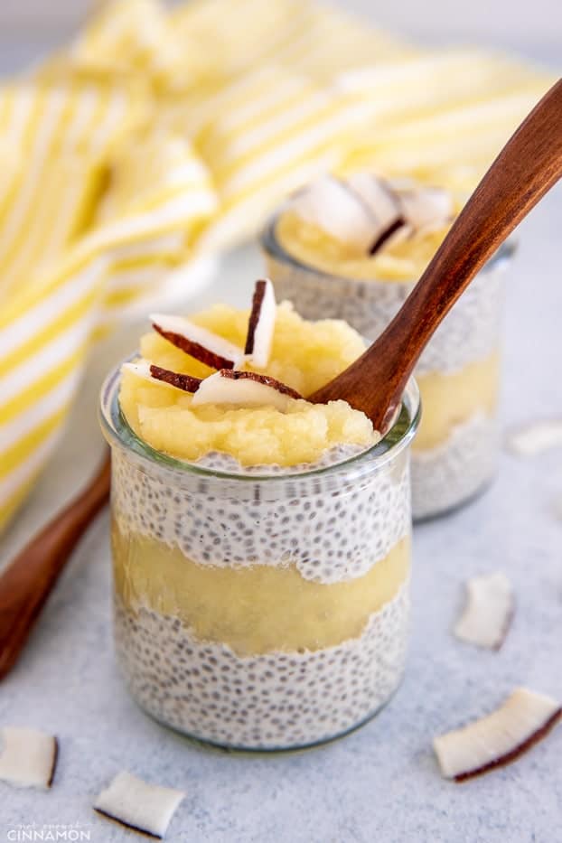 a glass of coconut pineapple chia pudding with a wooden spoon