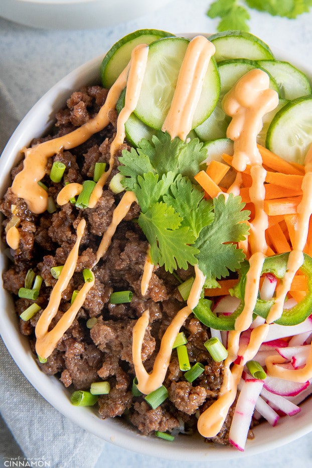 close-up of banh mi rice bowl drizzled with sriracha mayo and served with vegetables