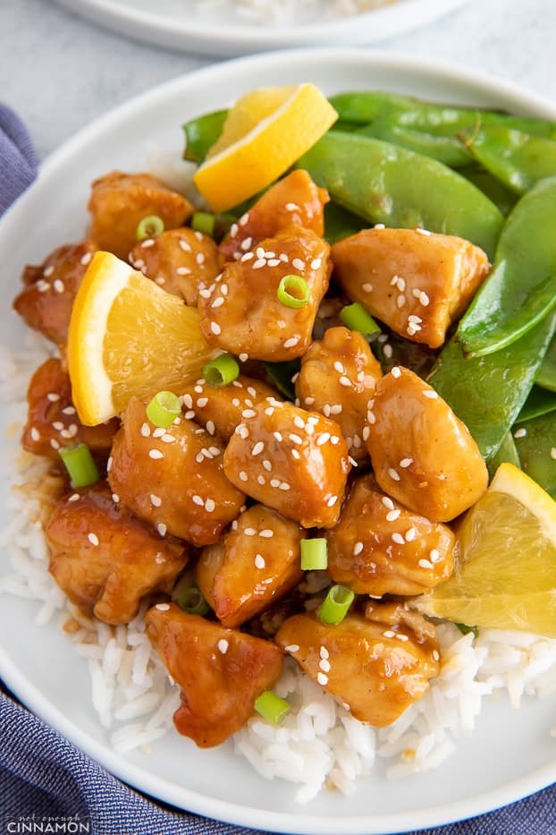 Chinese restaurant style sticky orange chicken served over a bed of rice with a side of snow peas 