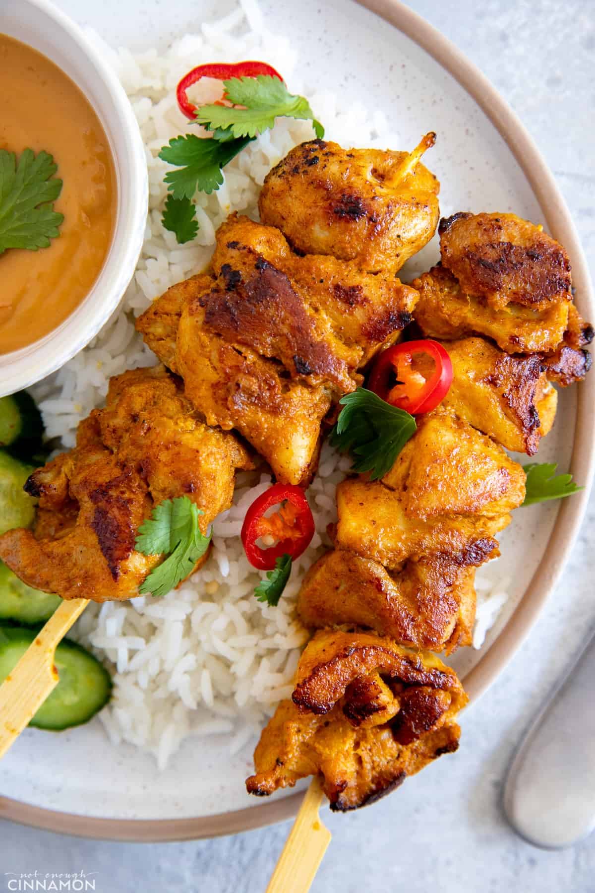 two juicy marinated Thai style chicken skewers served on a bed of rice with a side of peanut sauce 
