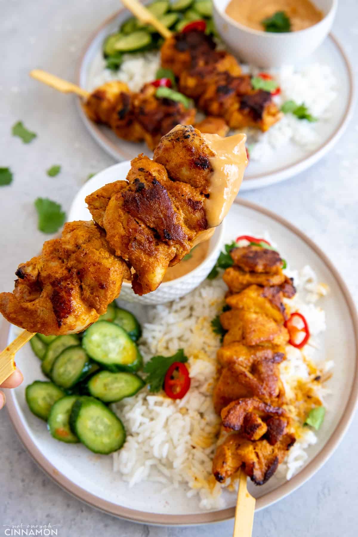 a hand holding a Thai chicken skewers that was dipped in peanut sauce 