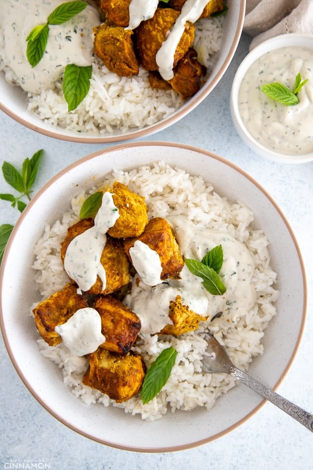 a bowl with rice topped with tandoori chicken and drizzled with yogurt dip 