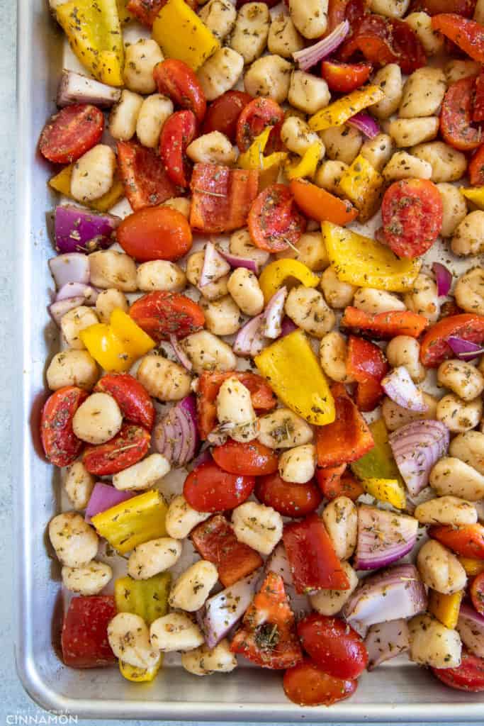gnocchi and vegetables tossed with Italian herbs and olive oil being spread onto a baking sheet 