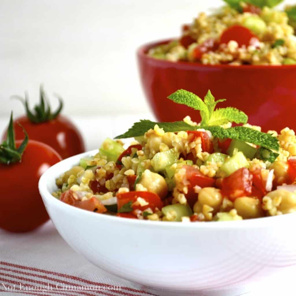 Summer Bulgur Salad with cucumbers, chickpeas and tomatoes decorated with fresh mint and served in two bowls with tomatoes on the side