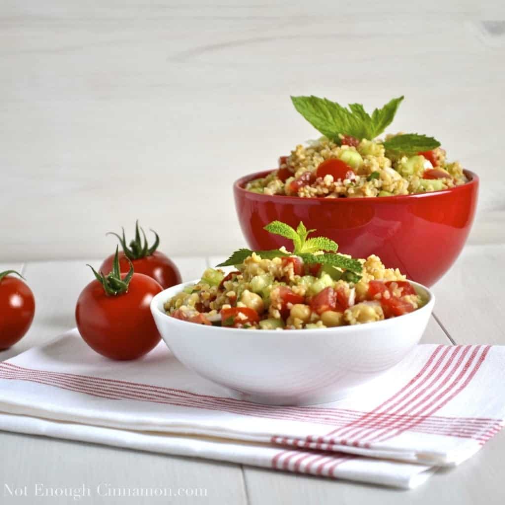 Summer Bulgur Salad with cucumbers, chickpeas and tomatoes decorated with fresh mint and served in two bowls with tomatoes on the side