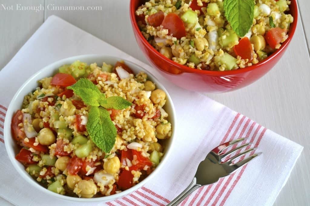 overhead shot of Summer Bulgur Salad with cucumbers, chickpeas and tomatoes decorated with fresh mint and served in two bowls placed on a white and red kitchen towel