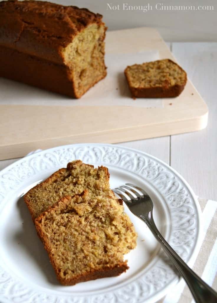 two slices of moist banana bread on a white plate with a loaf of best banana bread in the background