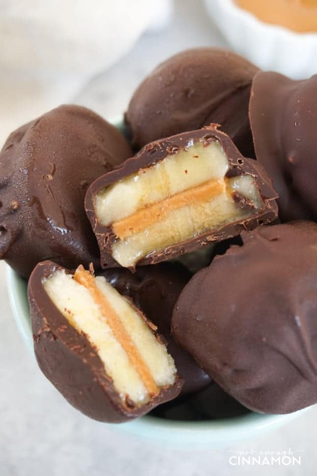 A picture showing a few frozen chocolate peanut butter banana bites in a small turquoise bowl, including one bite open in half to show the inside.