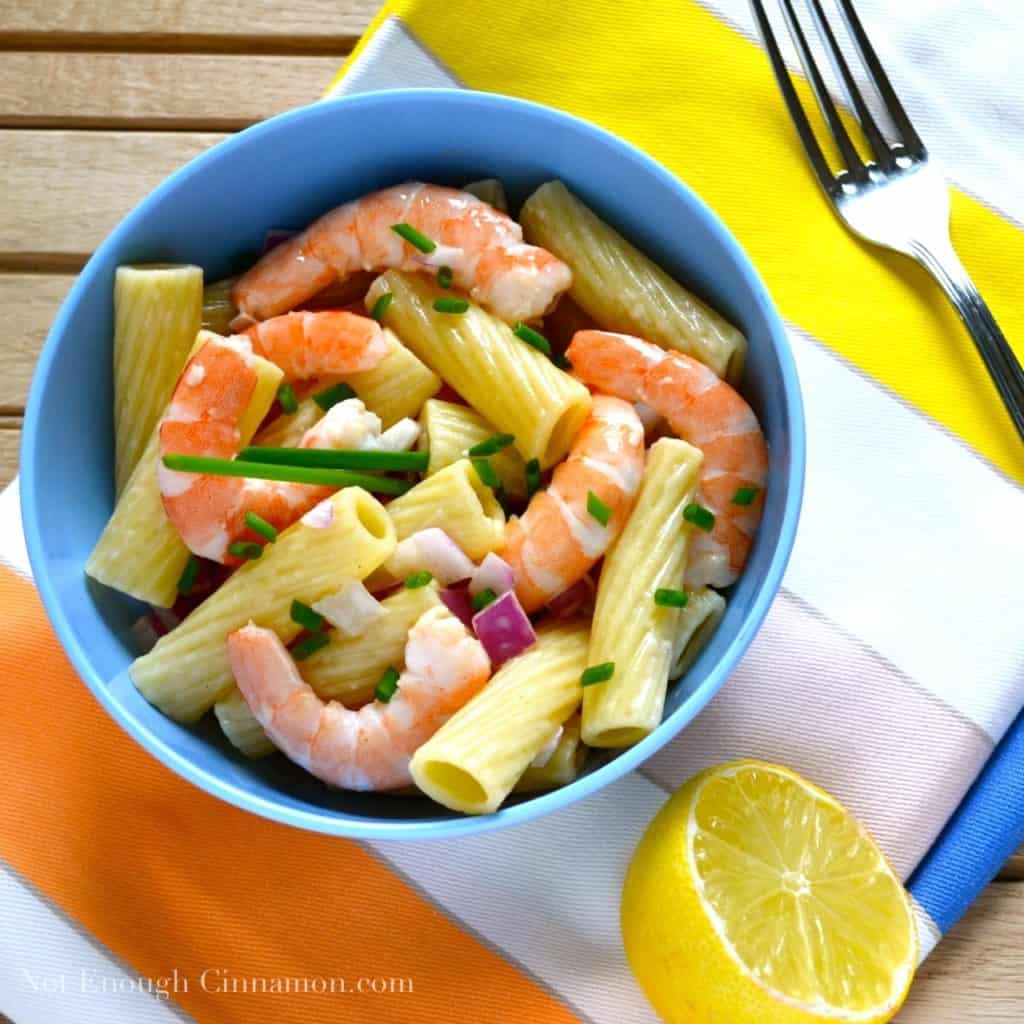 overhead shot of pasta salad with cooked shrimps, chopped red onions and chives in a light mayo dressing served in a blue bowl with half a lemon as decoration