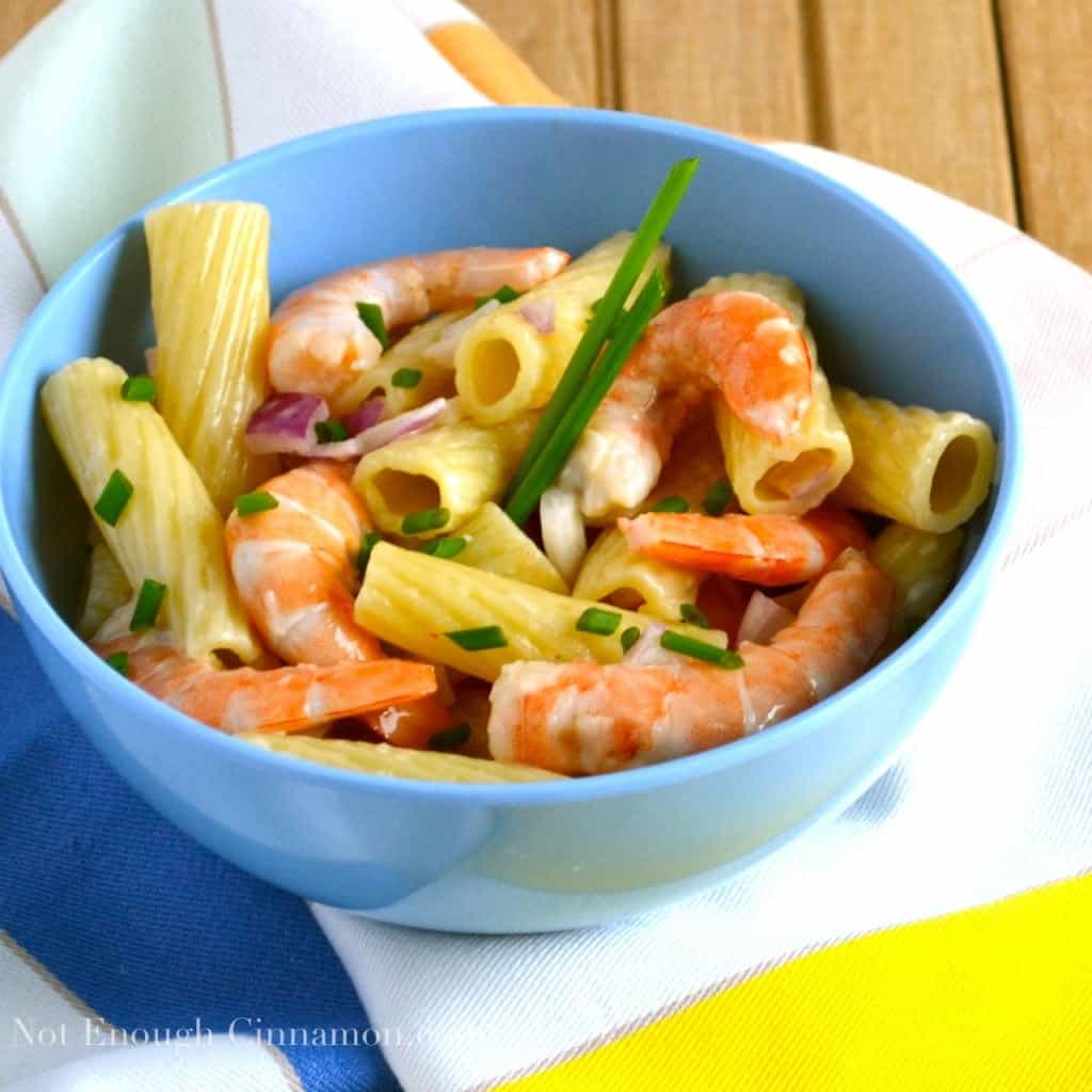 side view of rigatoni pasta salad with cooked shrimps, chopped red onions and chives in a light mayo dressing served in a blue bowl on a colorful napkin