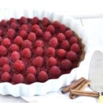 Raspberry Tart with Cinnamon Crust in a white tart dish with some cinnamon sticks on the side