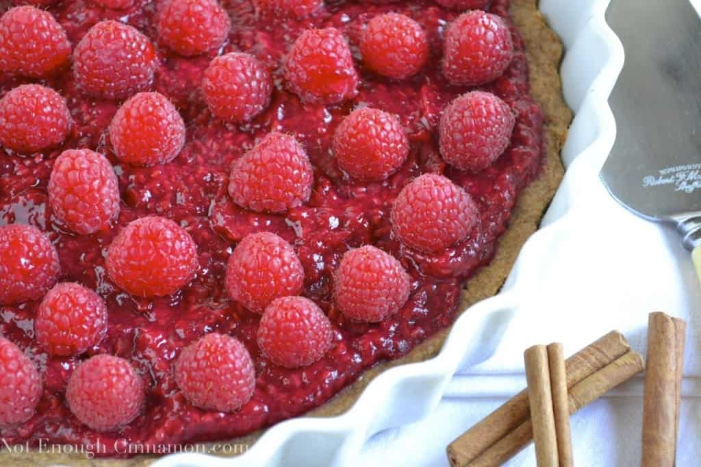 Skinny Raspberry Tart on whole wheat cinnamon crust in a white tart dish with some cinnamon sticks on the side