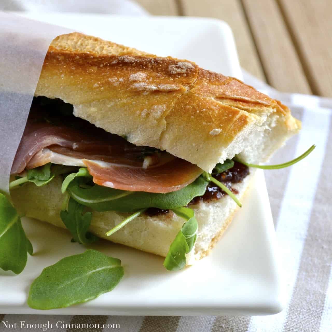 Prosciutto Sandwich with Pesto, Arugula and Fig Chutney wrapped in sandwich paper and served on a white plate