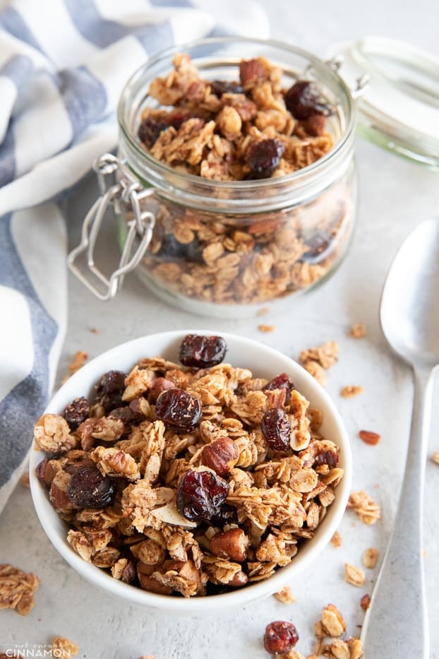 Granola is a small bowl and glass container with a stripped kitchen towel