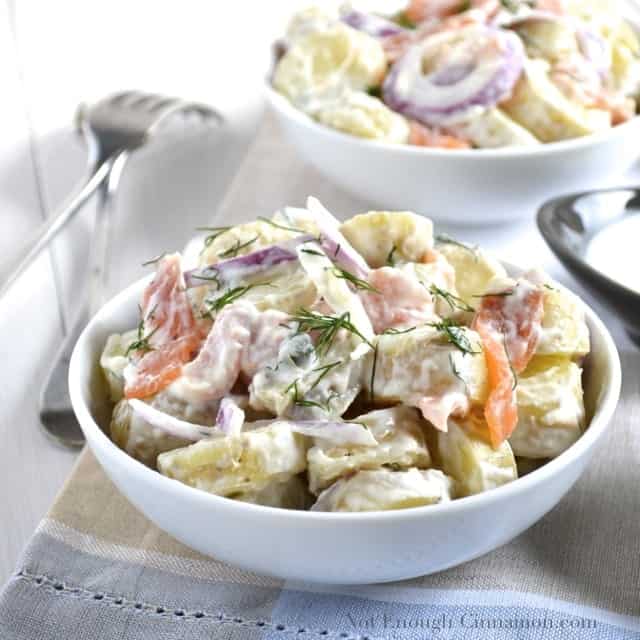 Smoked Salmon Potato Salad with a creamy dill dressing and topped with fresh dill served in 2 white bowls with 2 forks on the side