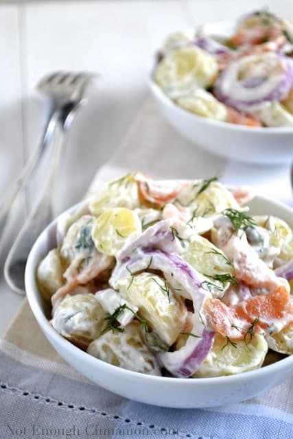 Smoked Salmon Potato Salad with a creamy dill dressing topped with fresh dill served in 2 white bowls with 2 forks on the side