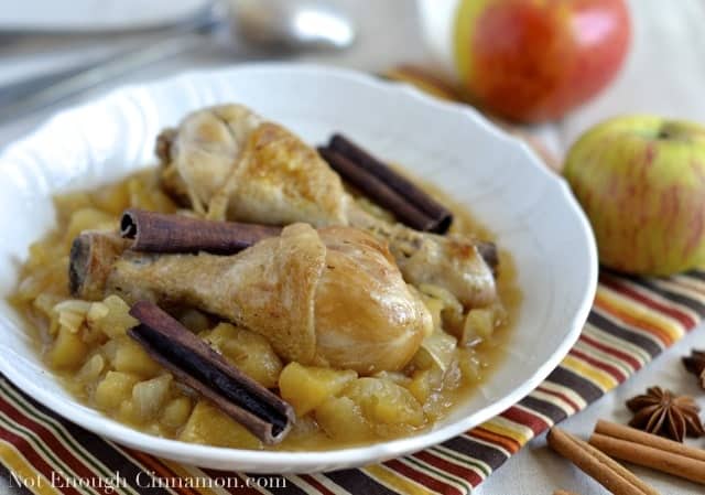 Chicken Stew with Apples and Cinnamon served in a white bowl with cinnamon bark as decoration and some apples in the background