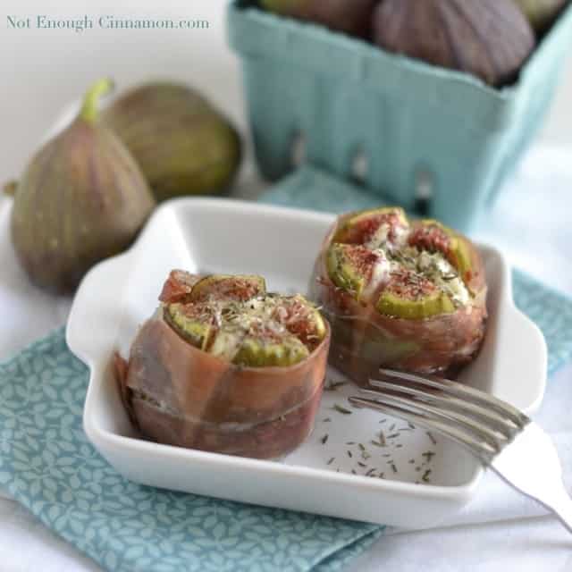 Goat Cheese Stuffed Figs wrapped in prosciutto served in a little white ramekin with some fresh figs in the background