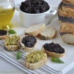Black Olive Tapenade served on slices of crunchy baguette with a tapenade filled dish in the background