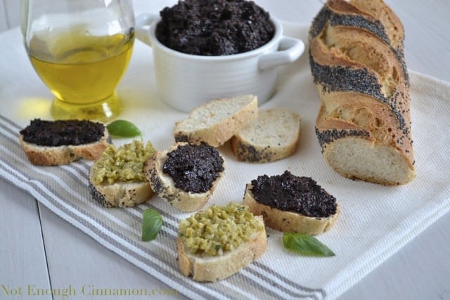 Black Olive Tapenade served on slices of crunchy baguette with a tapenade filled dish in the background