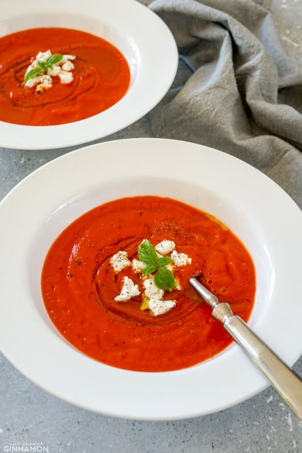Roasted bell pepper soup in a shallow white plate with a silver spoon