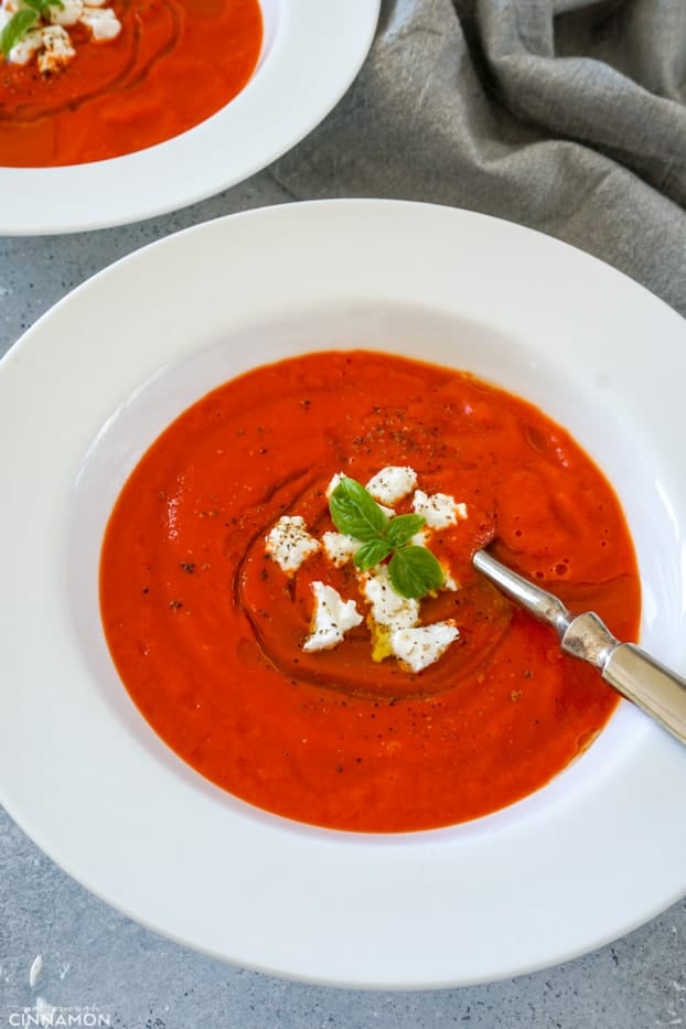 Bell pepper soup in a white plate with goat cheese topping and a drizzle of olive oil
