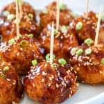 Asian glazed meatballs on a round white plate with toothpicks.