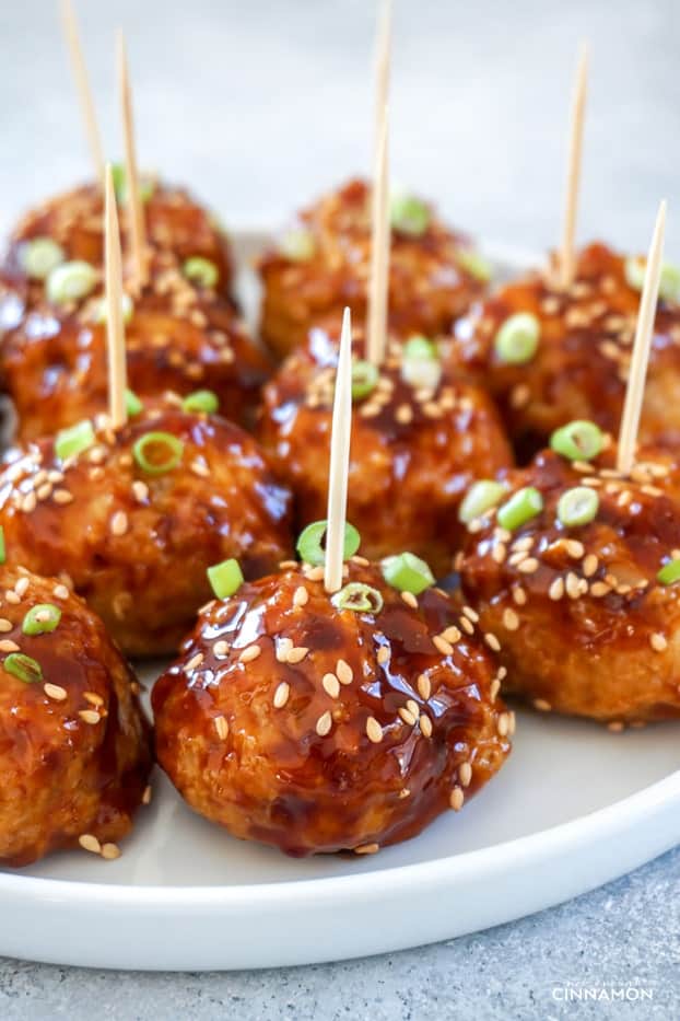 Asian glazed meatballs on a round white plate with toothpicks.