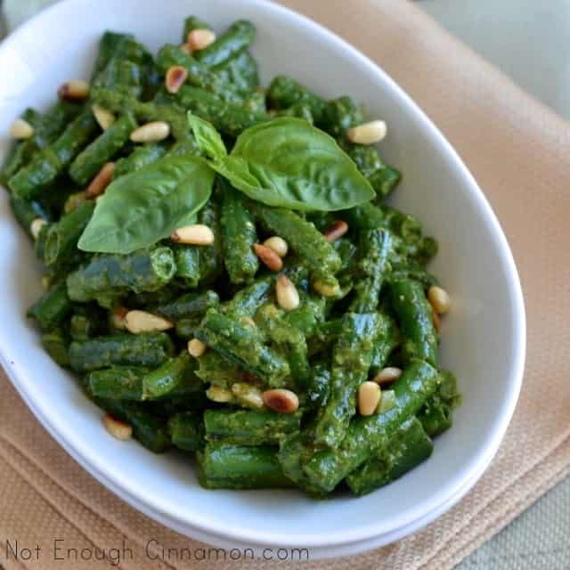 overhead shot of Crispy Green Beans with Pesto served in a white oval dish garnished with fresh basil and toasted pine nuts