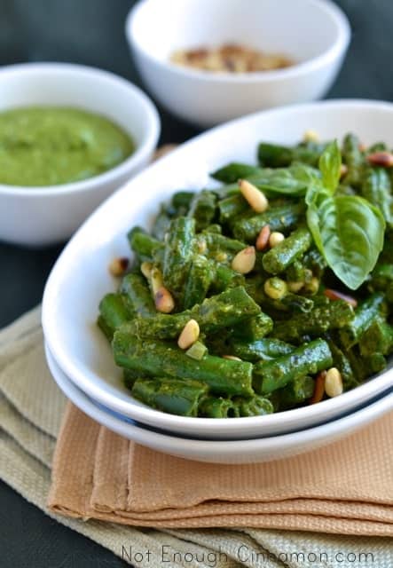 Close-up of Crispy Green Beans with Pesto served in a white oval dish with 2 little side dishes with toasted pine nuts and pesto