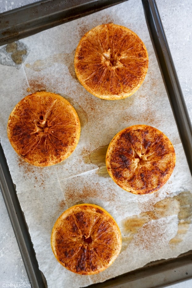 Four baked half grapefruits on a line baking sheet.