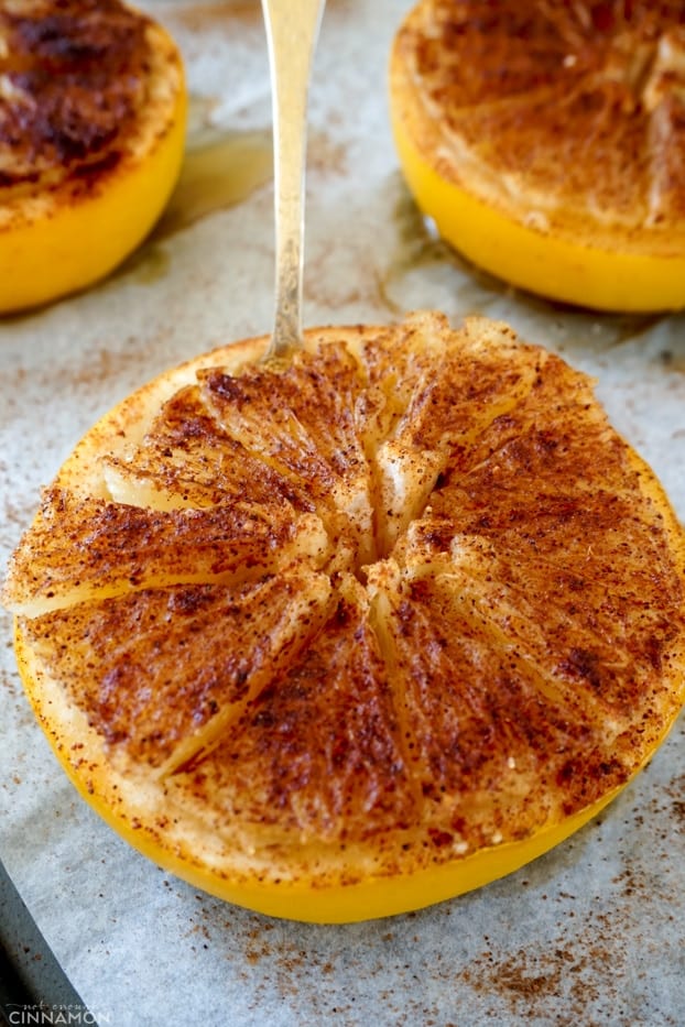 A baked half grapefruit with a golden spoon on a baking sheet