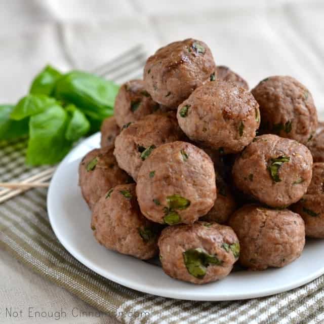 Ricotta Basil Meatballs piled up on a white plate served on a napkin with some basil on the side