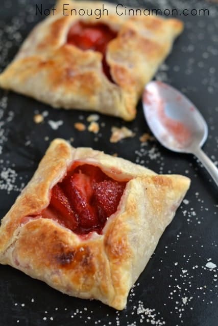 2 mini strawberry pies on a black tabletop sprinkled with some granulated sugar
