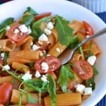 Pasta Risotto in a white bowl sprinkled with feta cheese, tomatoes and fresh arugula