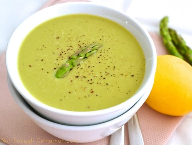 Skinny Cream of Asparagus Soup served in a white bowl with a lemon and some green asparagus on the side