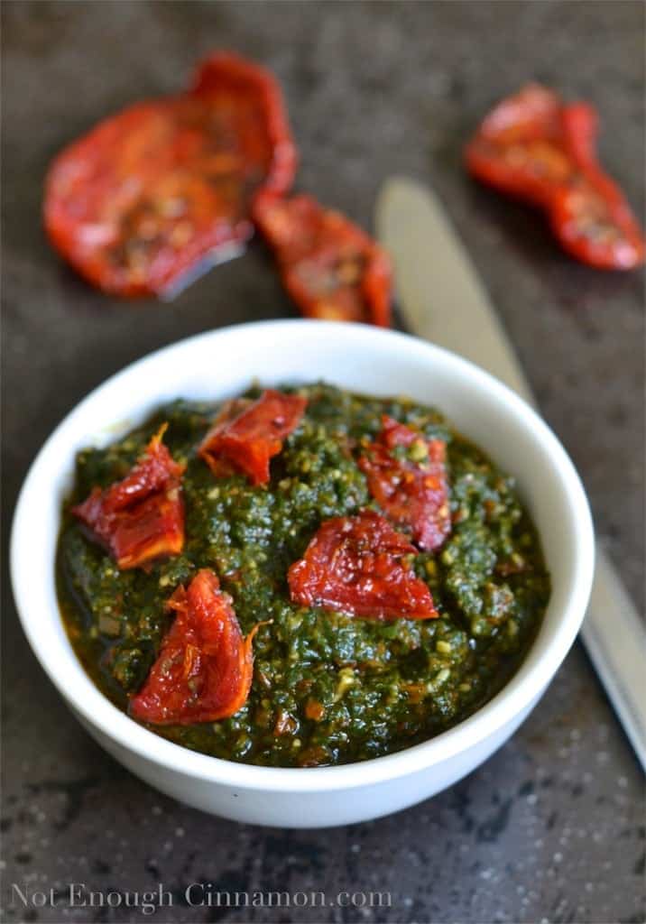 Basil and Sun-dried Tomatoes Pesto in a small white bowl with some sun-dried tomatoes in the background