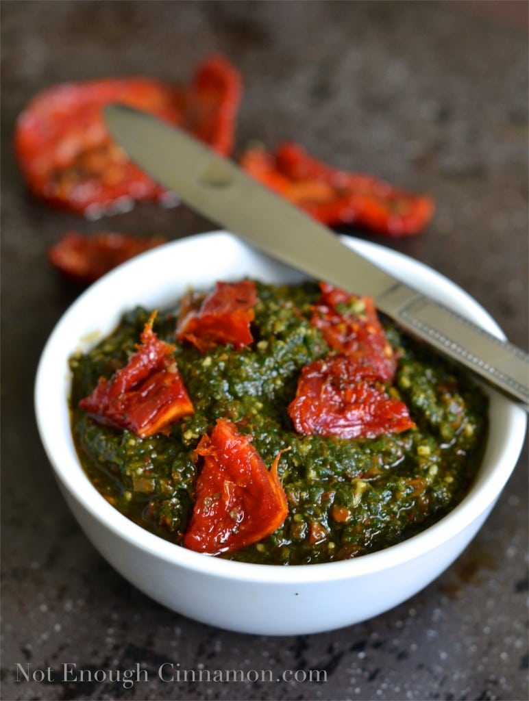Basil and Sun-dried Tomatoes Pesto in a small white bowl with some sun-dried tomatoes in the background