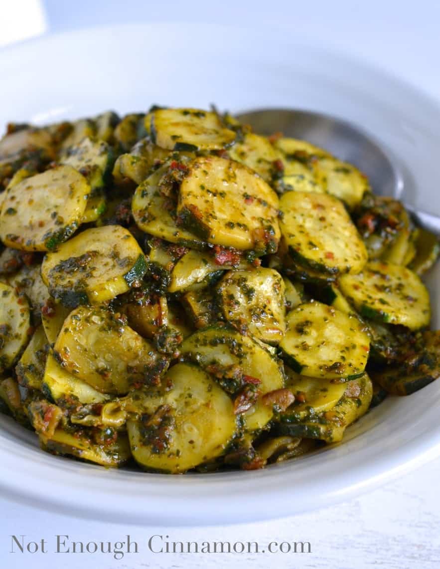 close-up of Lemon and Pesto Zucchini served in a white oval bowl with a big silver spoon on the side