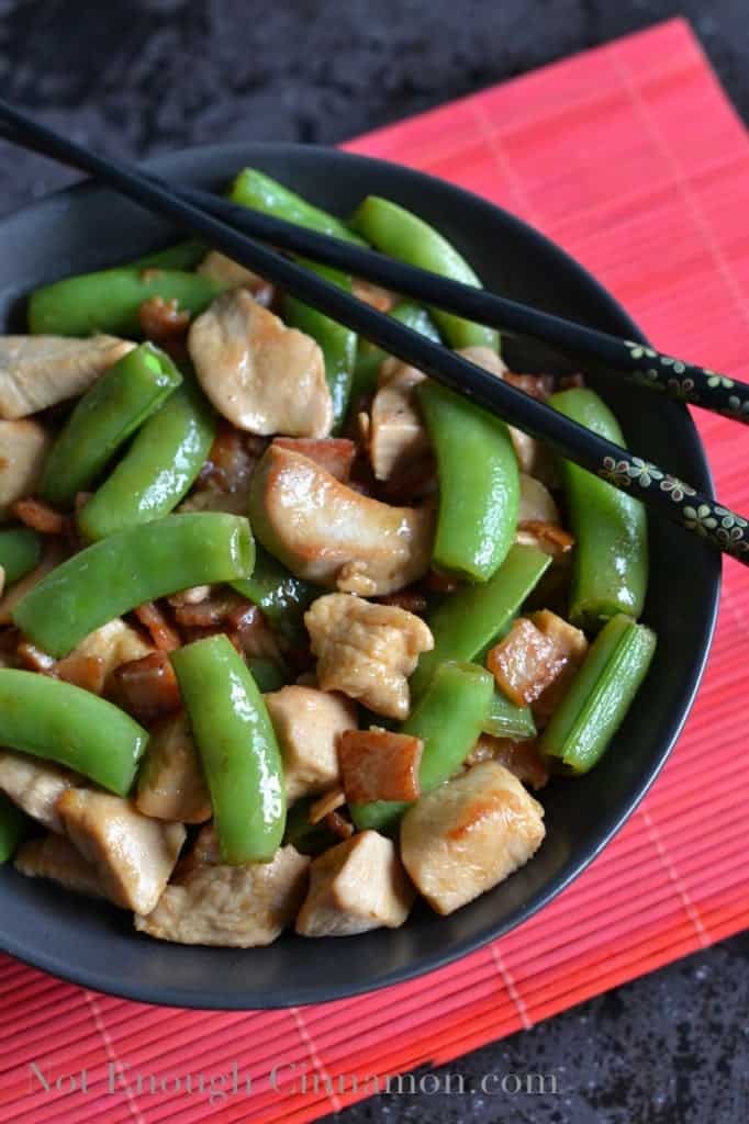 Bacon, Chicken and Snow Peas Stir-Fry served in a black bowl with some chopsticks on the side