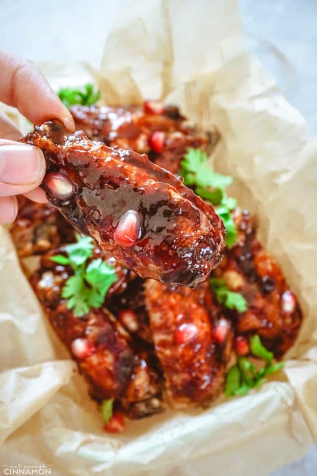 A pomegranate glazed chicken wings held by fingers