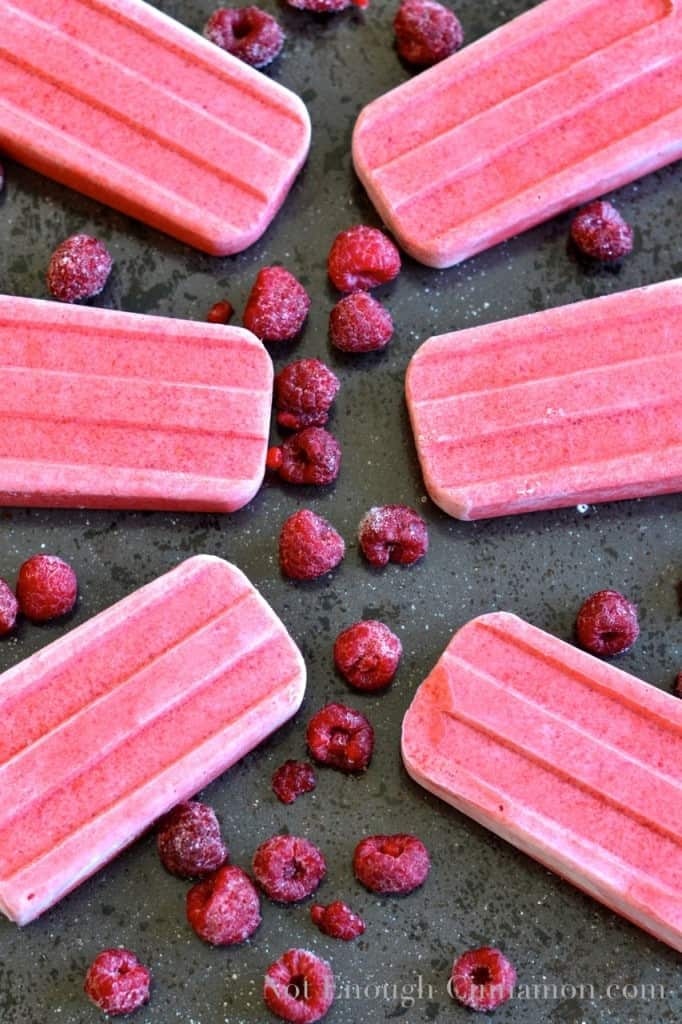 Coconut Berry Popsicles on a black tabletop surrounded by fresh raspberries